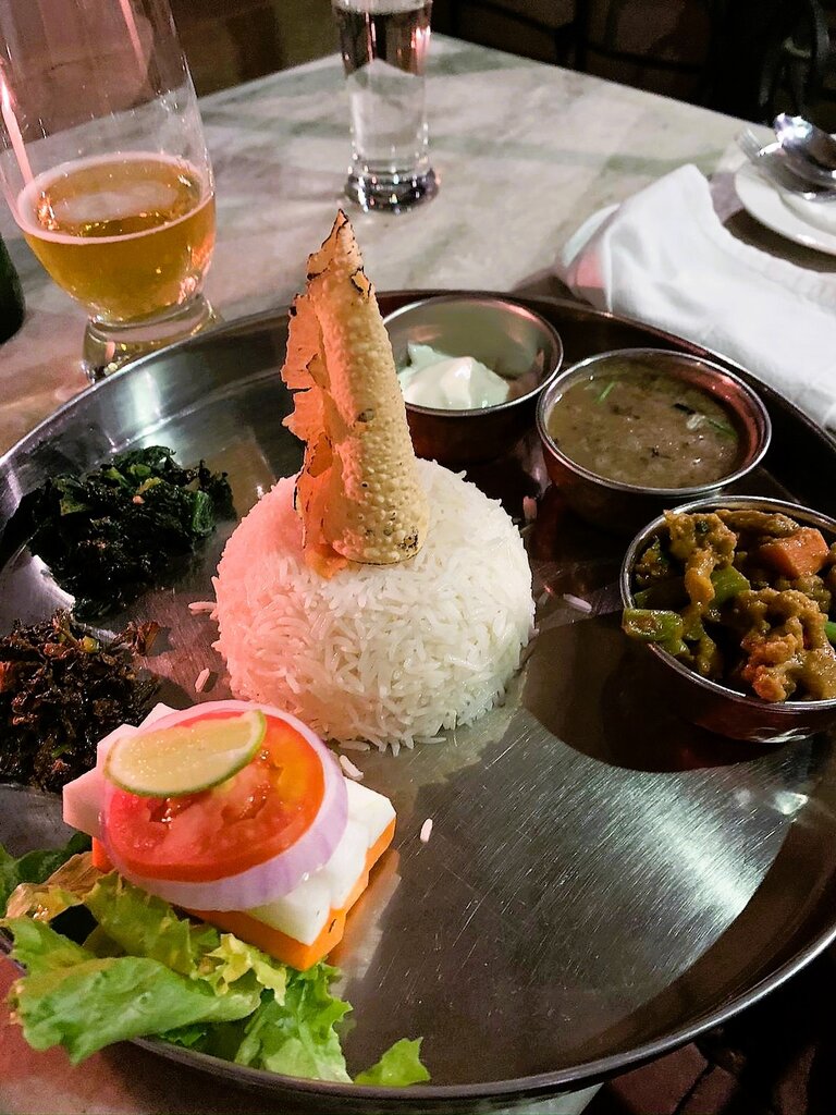 Traditionelles Nepali Food bestehend aus Currys, Gemüse, Salat und Reise auf einem silbernem Tablett serviert. Im Hintergrund steht ein Bier. | © Constanze Schwarz
