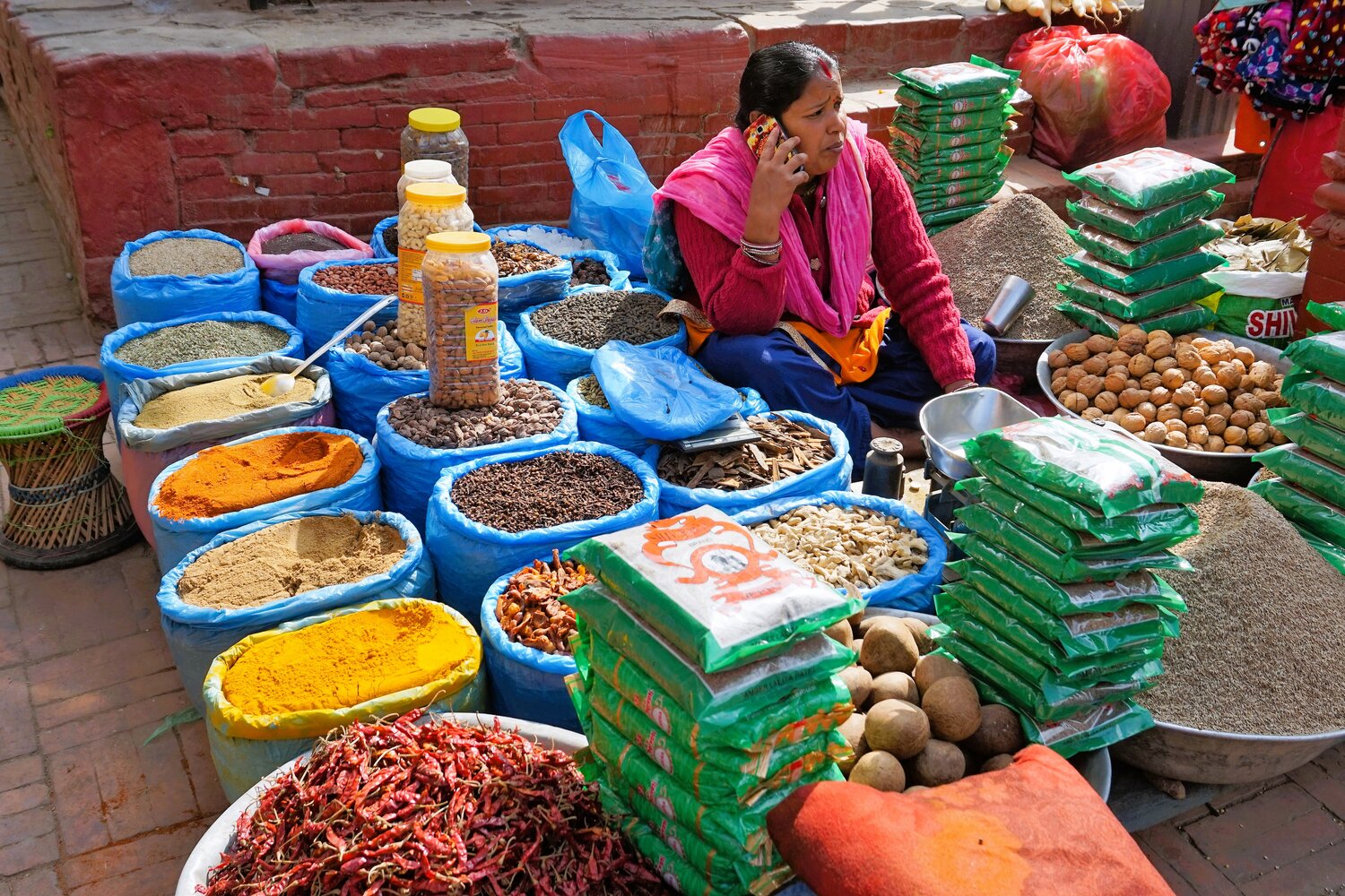 Gewürzhändlerin sitzt in ihrem Marktstand umgeben von Säcken und Päckchen mit bunten Gewürzen. | © Constanze Schwarz
