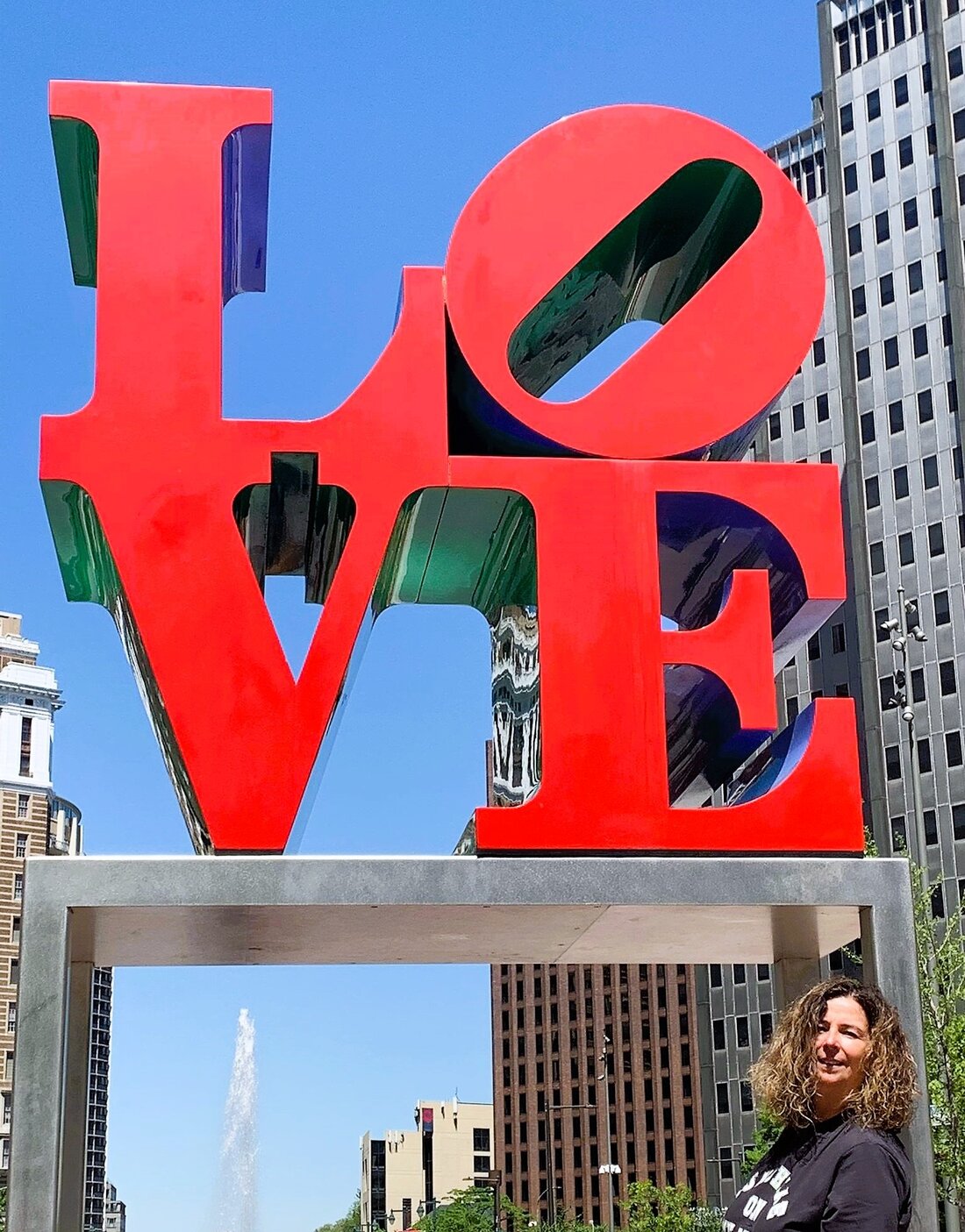 Constanze lehnt entspannt an der berühmten Love Statue im Love Park mit Hochhäusern im HIntergrund. | © Constanze Schwarz