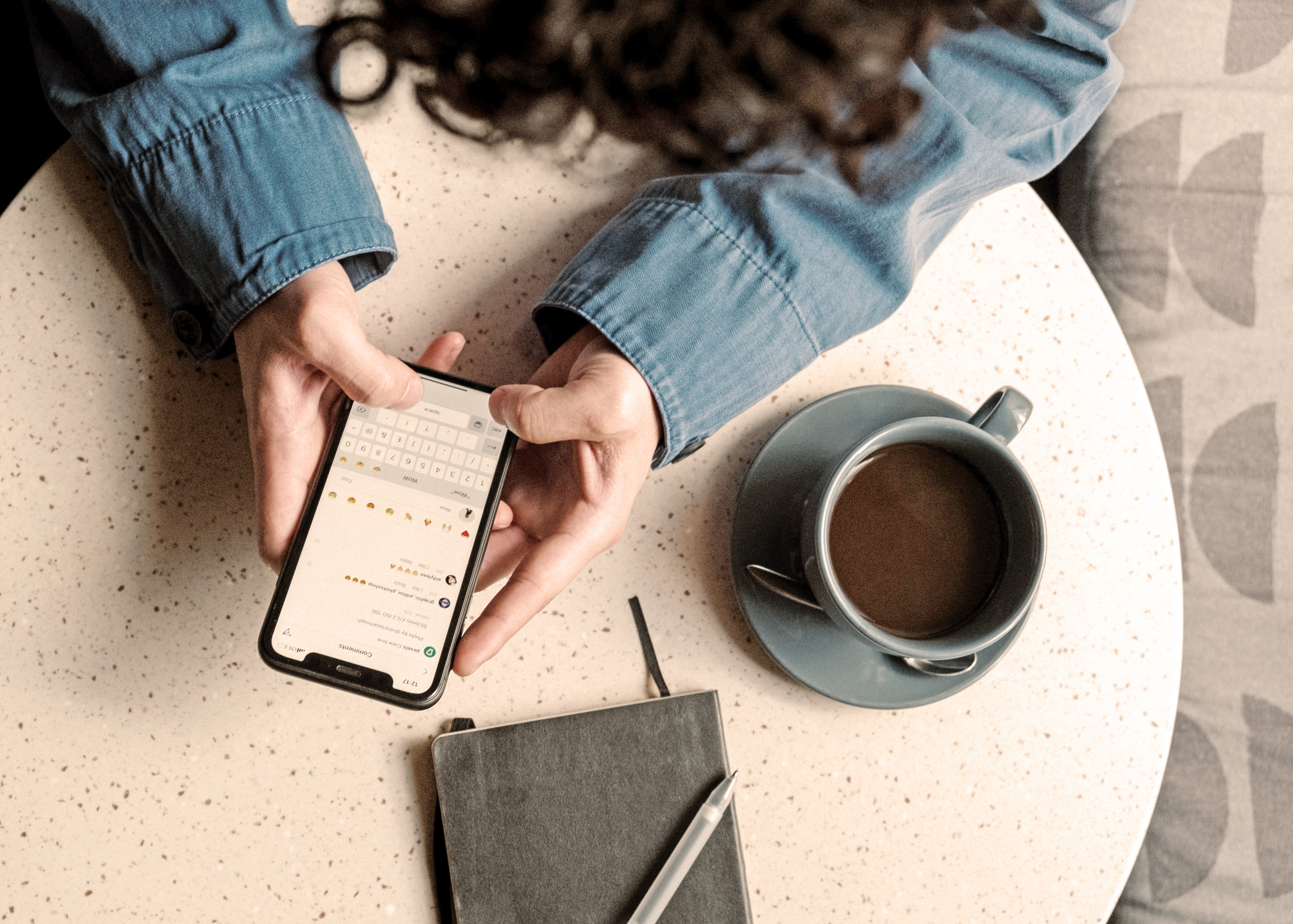 Blick von oben auf einen runden Tisch mit einer Kaffeetasse, eine Frau sitzt am Tisch und tippt Nachrichten auf ihrem Smartphone. | © pexels.com | Cottonbro Studio